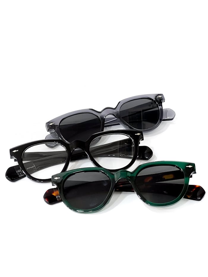 Flat lay of three stylish sunglasses with black and green frames on white background.