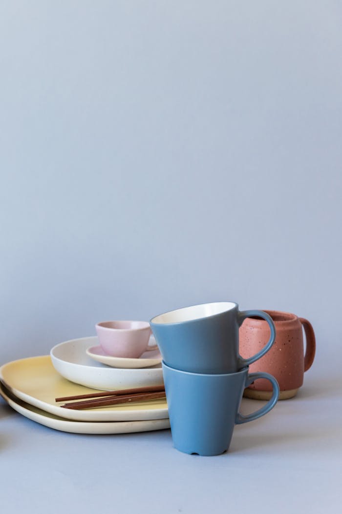 A stylish arrangement of ceramic dinnerware with pastel cups and chopsticks on a blue background.
